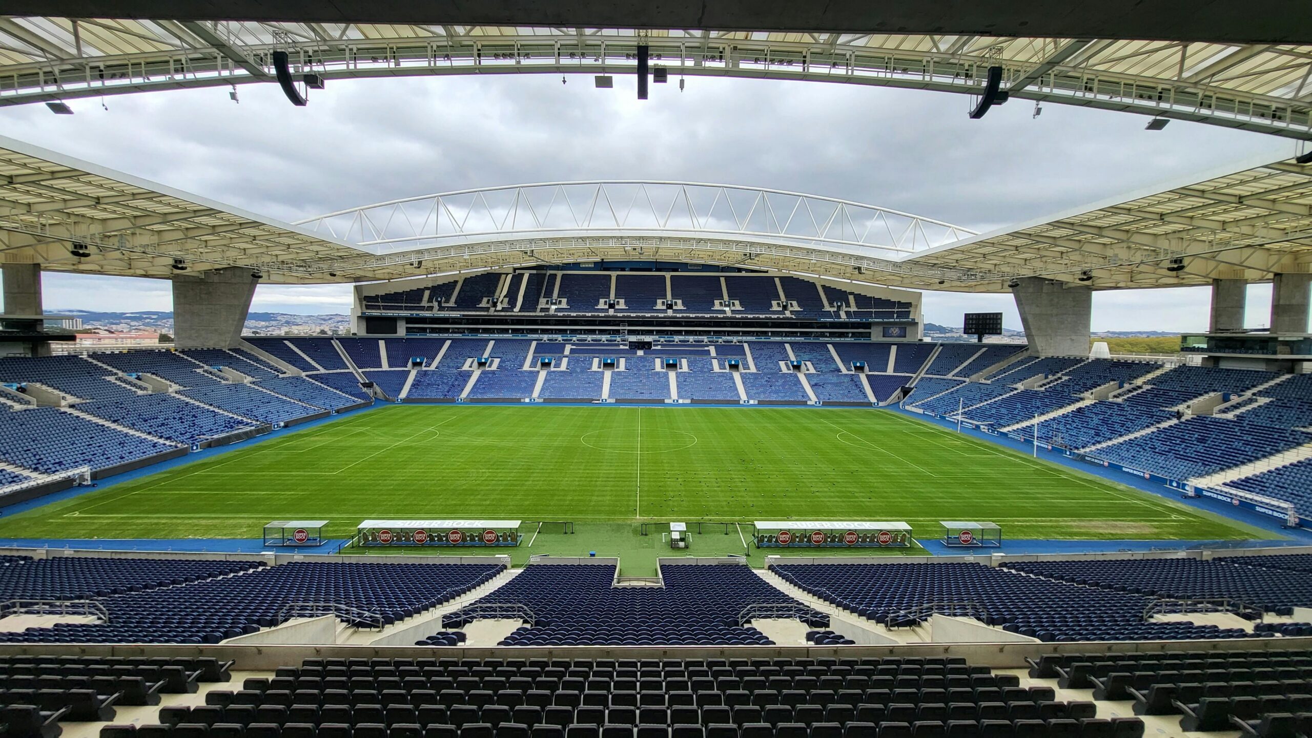 A panoramic view of an empty football stadium with green field and blue seating.